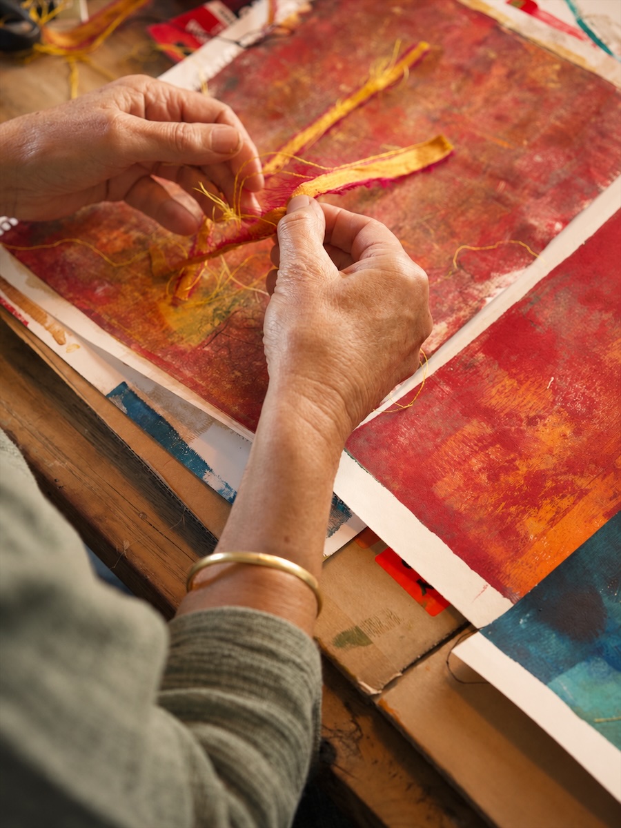 De handen van Els leggen gele draden op een rood werk op papier